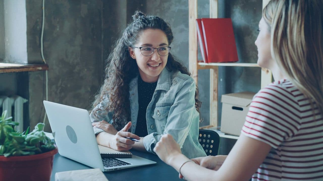 A career adviser with a laptop talks with a young woman across a desk